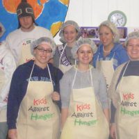 Students in hairnets and aprons in a group photo working at Kids Against Hunger