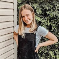 Female standing with hands on hips and smiling at the camera.