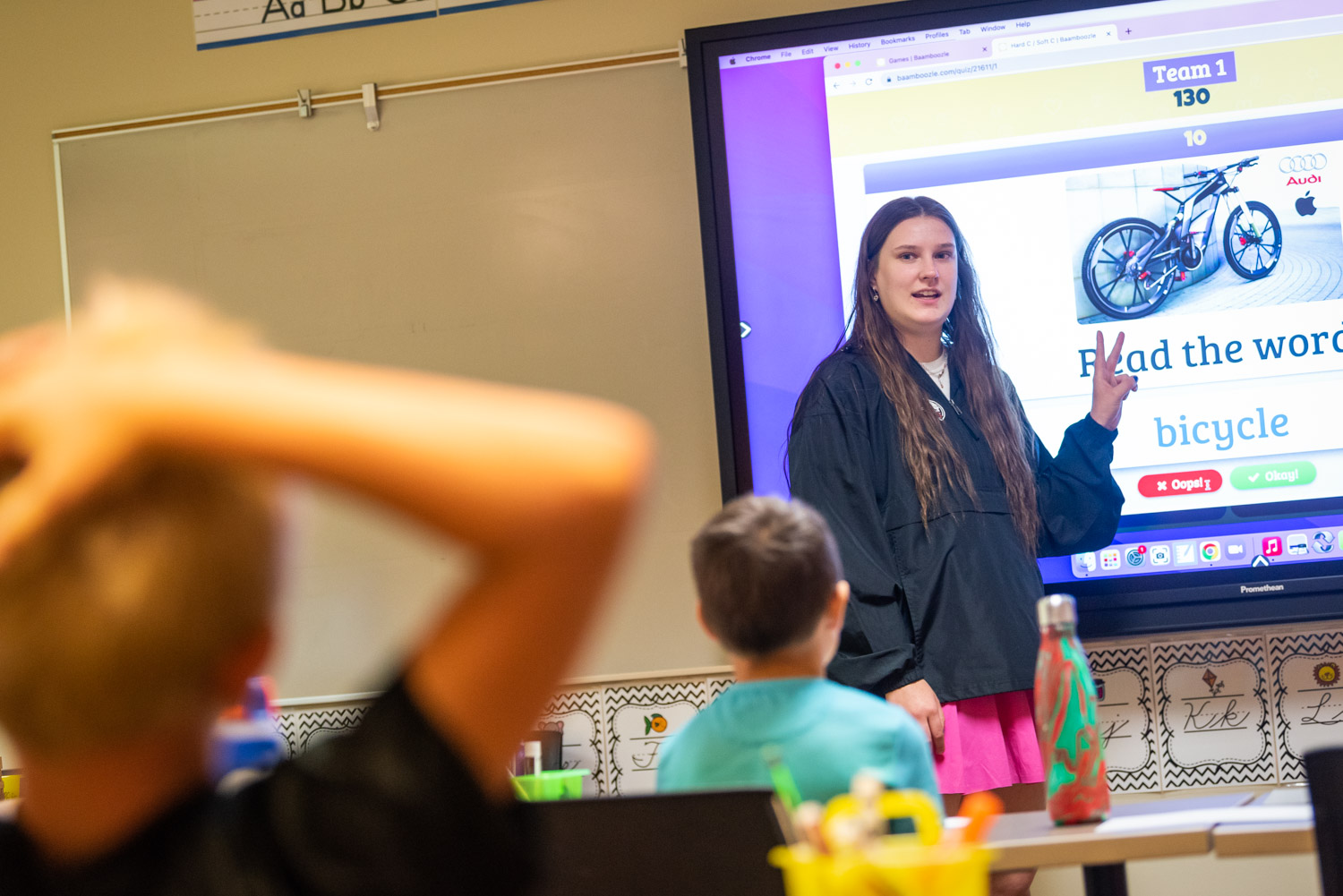 Teacher by tv screen looking at students from front of the room