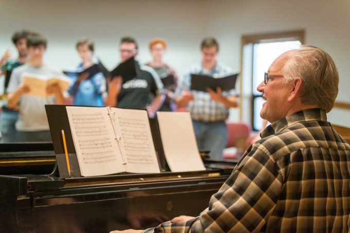 Music director at piano smiling at students