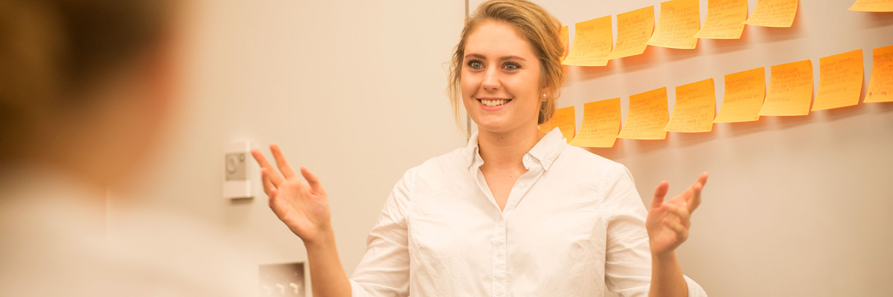 Female student presents in front of white board with yellow sticky notes on it