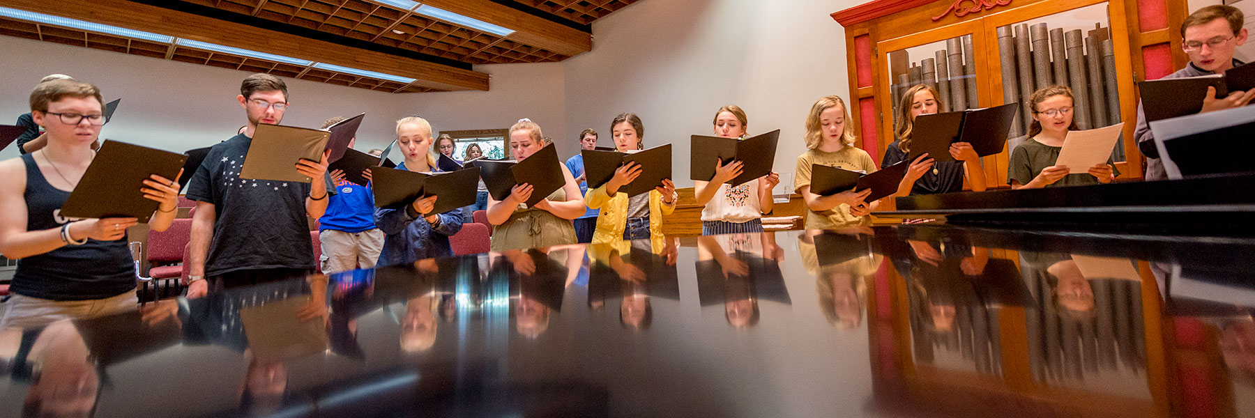 choir singers around piano holding notebooks