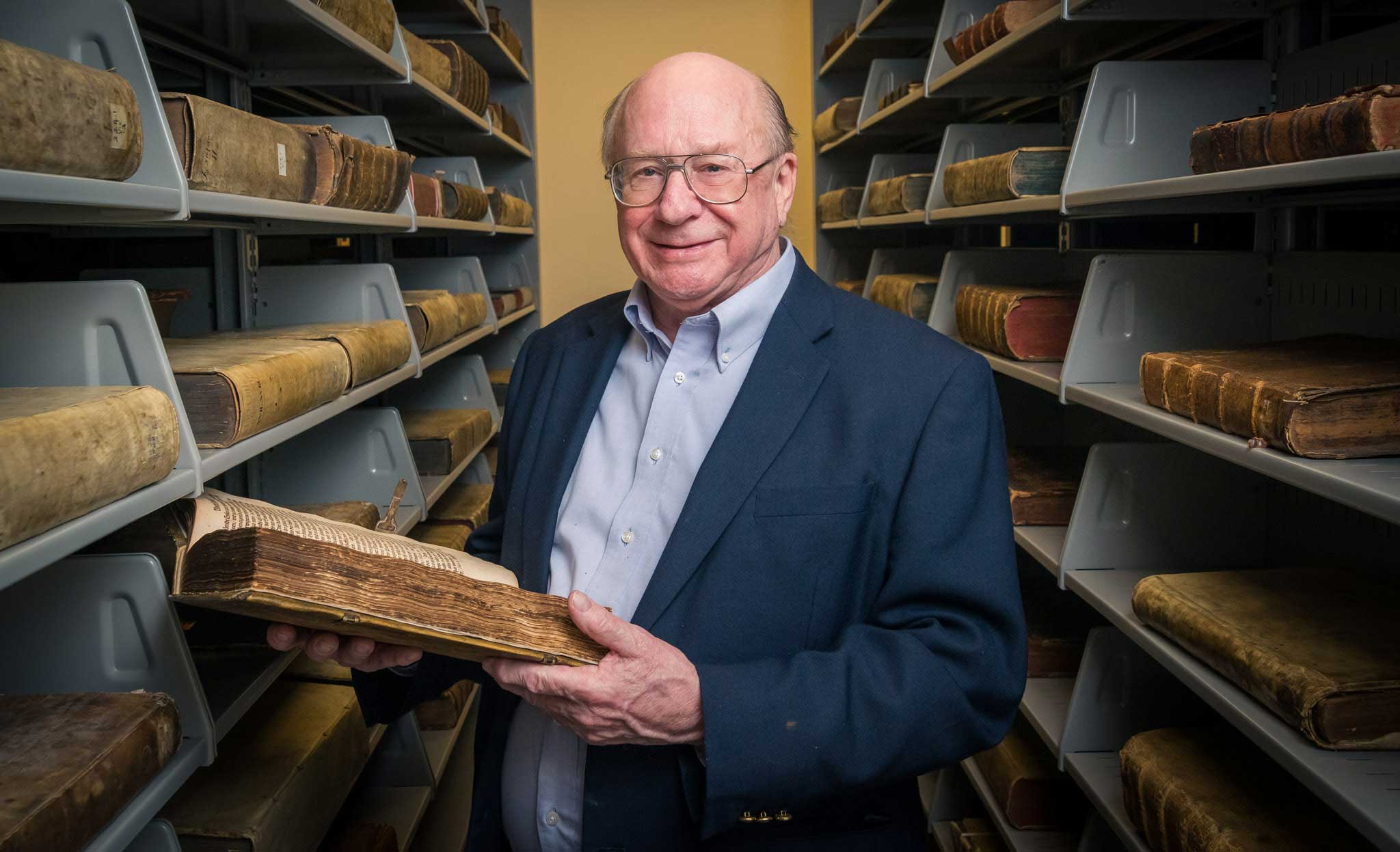 Erling Teigen among bookshelves holding old book