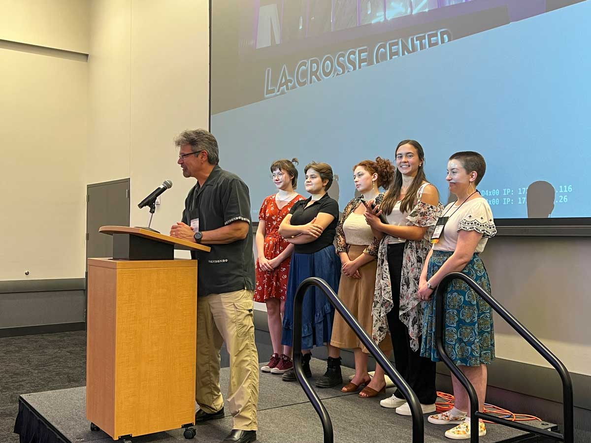 Group, adults, speaking, standing, art show, images, Rev. Terry Schultz, Lizzy Strackbein, Lydia Kratz, Maida Jaspersen, Abby Skorenkyi, BLC alumna Leah Kurth at the annual meeting of the WELS Lutheran Women’s Missionary Society in October 2023, Bethany Magazine