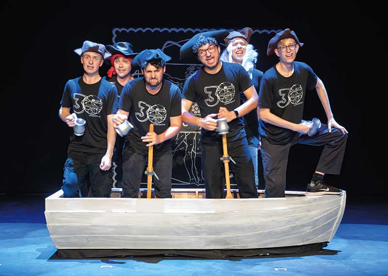 Male figures with pirate hats holding mugs while standing in small boat