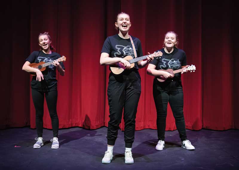 Three females with ukuleles on stage