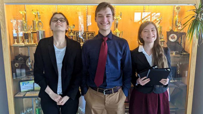 speech and debate students in front of trophy case