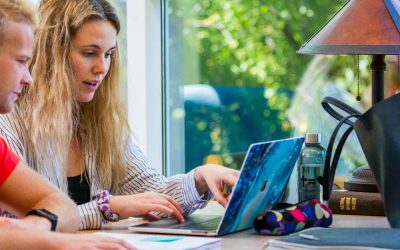 a male and female student look at a laptop on a desk while studying in memorial library