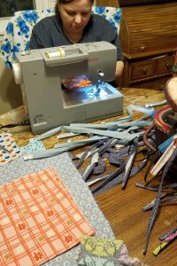 female sits at sewing machine with cloth strips and fabric on table in front of her