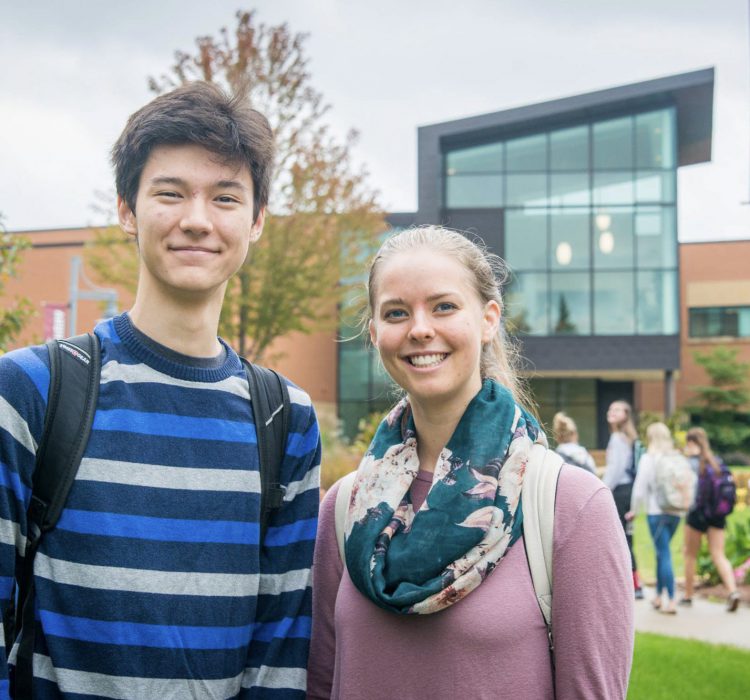 two students smiling at camera outside of academic building (Honsey Hall)